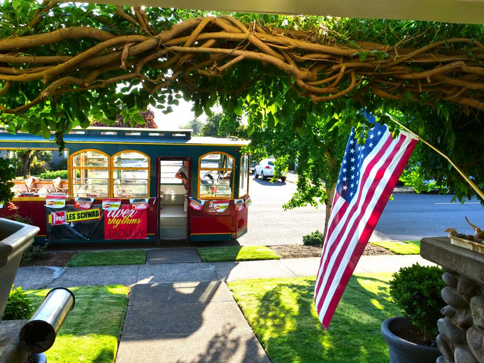Photo of a historic home porch looking out to antique trolley and American flag during the Albany Sumer Historic Home Tour
