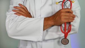 Photo of a healthcare professional in a white lab coat holding a red stethoscope 