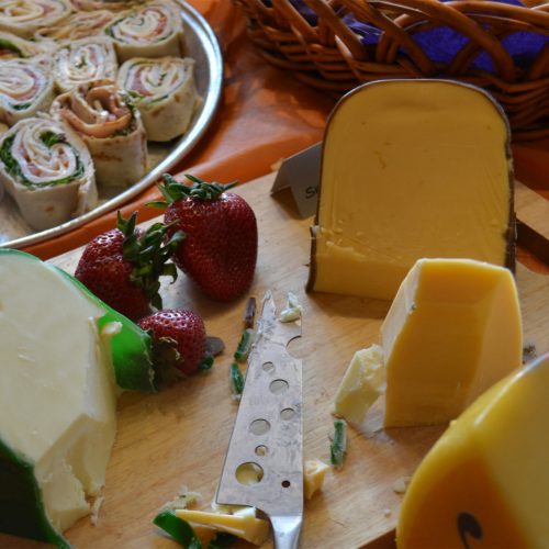 Photo of different cheeses on board with fruit.
